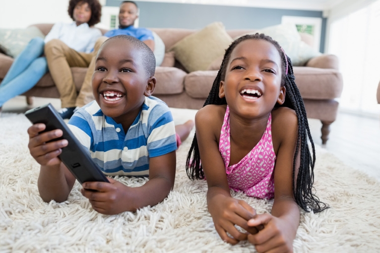 Two young children watching TV from the carpet, with their parents on the couch behind them